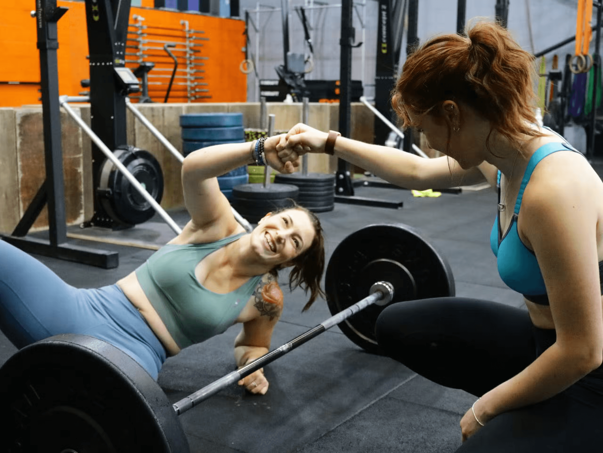 Two women fist bumping during a functional fitness workout in a gym.