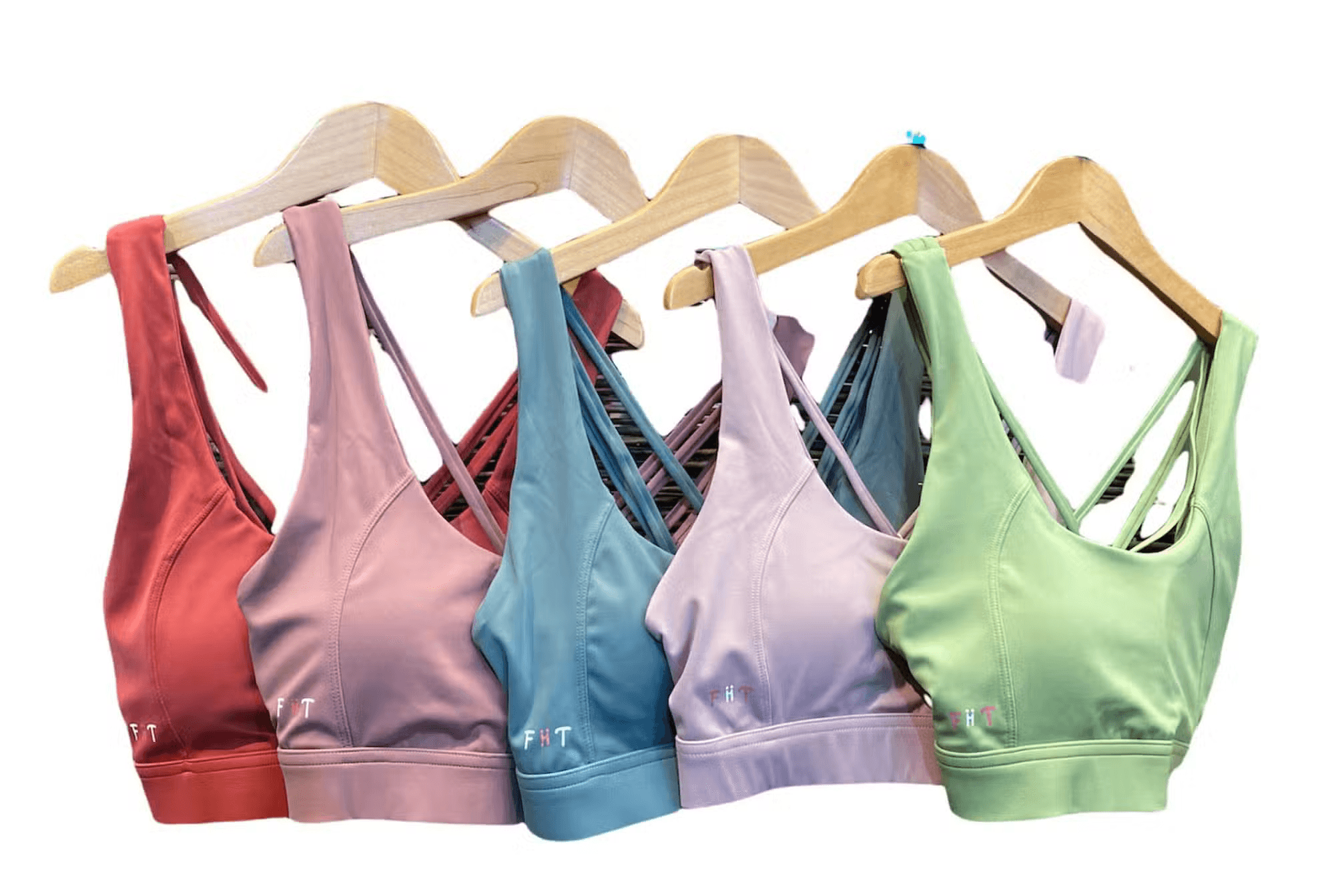 Pastel FiiTUK sports bras in different colours hanging on wooden hangers.